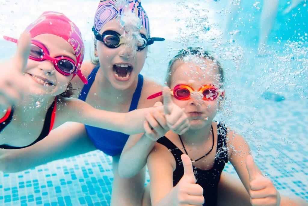 Unterwasserbild von 3 lachenden Kindern mit Schwimmbrillen im Schwimmbad